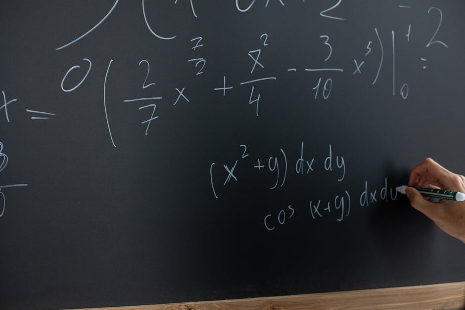 Hand writing mathematical equations on a chalkboard in a classroom setting.